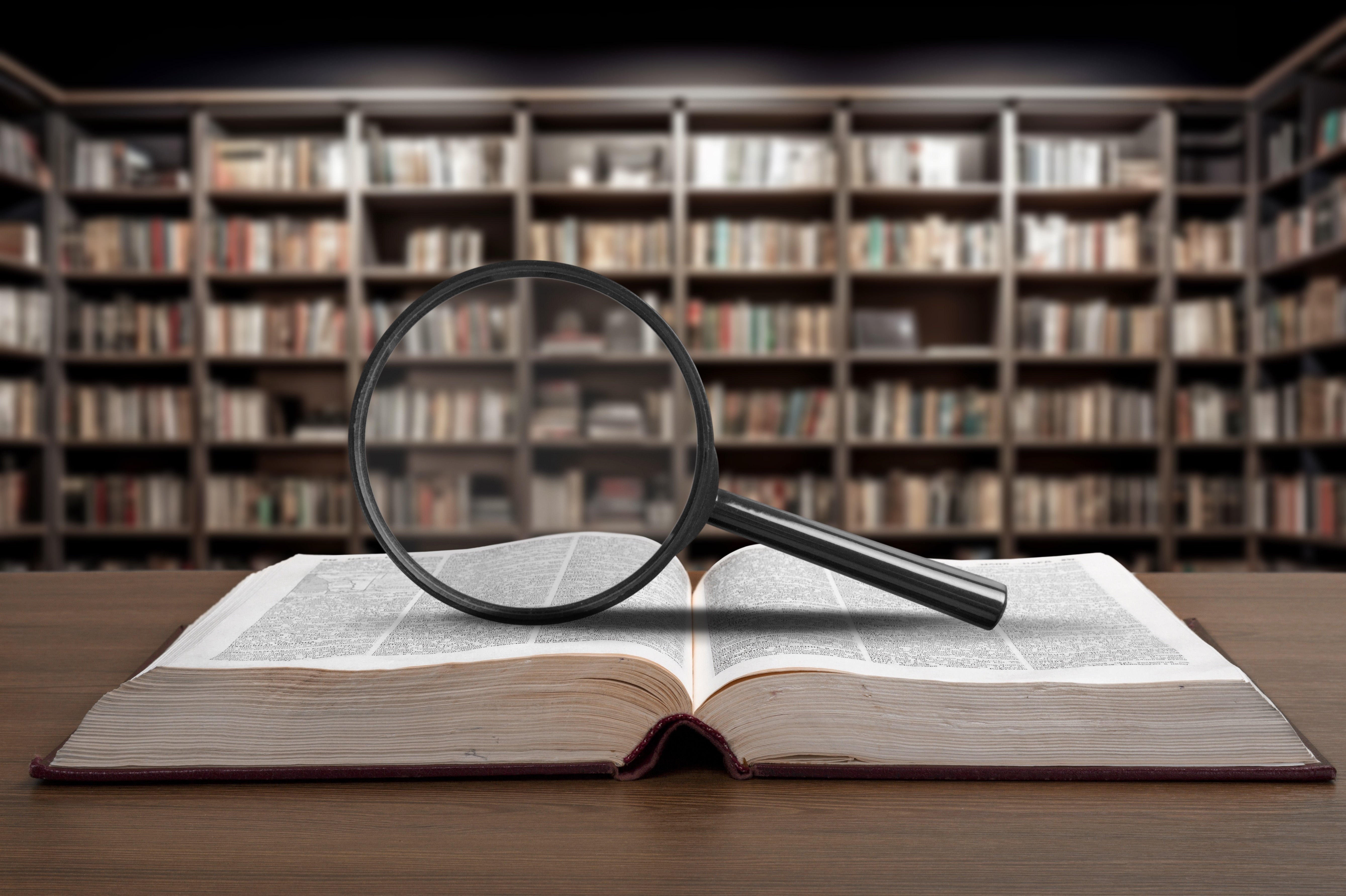 A magnifying glass resting on an open dictionary atop a dark wooden desk, symbolizing the clarity and expert translation Atypical Forte provides when demystifying complex B2B acronyms like GDS, TMC, and RFP for hoteliers.